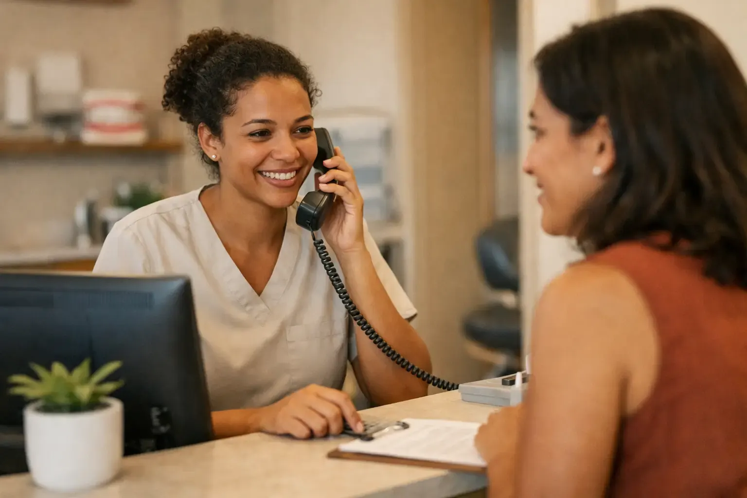 Recepcionista de clínica atendendo uma paciente no balcão com o telefone na mão